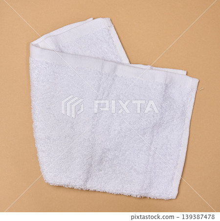 A folded white terry towel on a beige background. A folded white terry towel on a beige background. 139387478