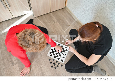 Two people playing chess on the floor in a home during daytime Two people playing chess on the floor in a home during daytime 139387522