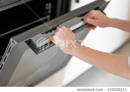 A hands open the door of a modern built-in oven. Concept of home cooking and appliance use. 139388211