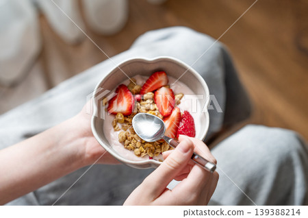 Close-up of a person holding a ceramic bowl with yogurt, fresh strawberries, and granola. Close-up of a person holding a ceramic bowl with yogurt, fresh strawberries, and granola. 139388214