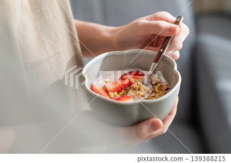 Healthy breakfast with yogurt, granola and fresh strawberries in a bowl, close-up hands 139388215