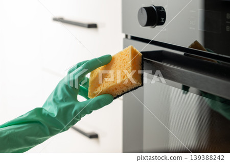 Cleaning the oven door with a sponge and a rubber glove, removing grease in a modern kitchen. 139388242