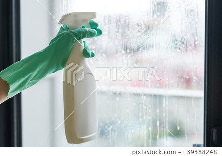 Window cleaning. A gloved hand sprays cleaning solution onto a window. House cleaning concept. Window cleaning. A gloved hand sprays cleaning solution onto a window. House cleaning concept. 139388248