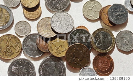 Assorted coins from various countries including silver, copper, and bronze, scattered on a white surface showcasing different denominations and designs Assorted coins from various countries including silver, copper, and bronze, scattered on a white surface showcasing different denominations and designs 139389190