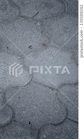 Gray interlocking pavement tiles with a textured surface and subtle imperfections, creating a uniform pattern on the ground in an outdoor setting Gray interlocking pavement tiles with a textured surface and subtle imperfections, creating a uniform pattern on the ground in an outdoor setting 139389202