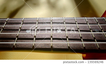 Close-up view of a guitar fretboard showcasing wooden texture, metal fret markers, and strings under natural light with a blurred background Close-up view of a guitar fretboard showcasing wooden texture, metal fret markers, and strings under natural light with a blurred background 139389246