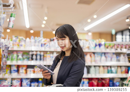 A businesswoman shopping at a supermarket while looking at notes on her smartphone. 139389255