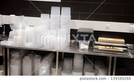 Plastic containers stacked on a stainless steel table in a food preparation area, with additional packaging materials visible in the background 139389260