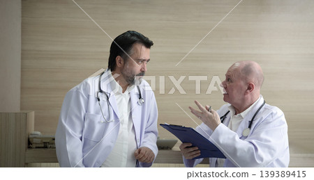 Doctors discuss. Two experienced doctors discussing patient information and medical reports in a hospital corridor. Professional healthcare teamwork consultation and collaboration in clinic hospital 139389415