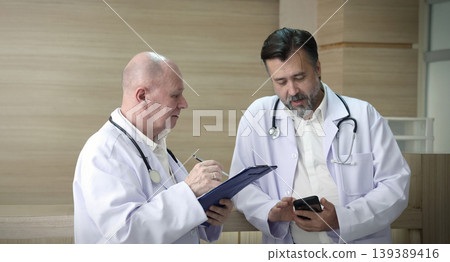 Doctors discuss. Two experienced doctors discussing patient information and medical reports in a hospital corridor. Professional healthcare teamwork consultation and collaboration in clinic hospital 139389416