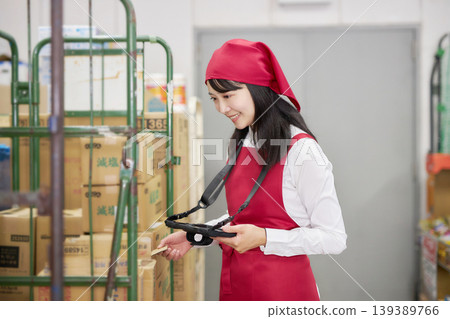 A young woman manages inventory using a tablet in the back room. A young woman manages inventory using a tablet in the back room. 139389766