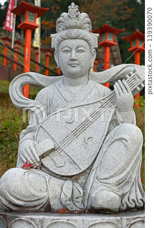 A statue of Benzaiten playing the biwa; a traditional temple scene woven together by vermilion lanterns and stone statues. A statue of Benzaiten playing the biwa; a traditional temple scene woven together by vermilion lanterns and stone statues. 139390070