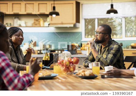 Family enjoying a weekend breakfast together in a sunny kitchen. Parents serve coffee, croissants and orange juice while children laugh, moment of love and happiness around the table. Family enjoying a weekend breakfast together in a sunny kitchen. Parents serve coffee, croissants and orange juice while children laugh, moment of love and happiness around the table. 139390167