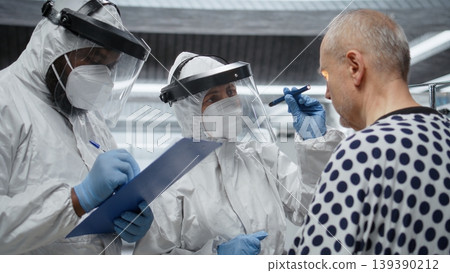 Doctor in isolation examines patient under biohazard conditions, recording treatment outcomes and immune response to support innovation and medical science in epidemic prevention. Camera A. 139390212