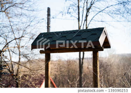 Wooden shelter structure with shingled roof standing outdoors in rural landscape with trees and sky background. Architecture and construction Wooden shelter structure with shingled roof standing outdoors in rural landscape with trees and sky background. Architecture and construction 139390253