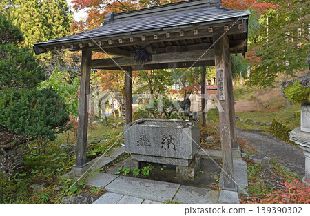 The water basin is enveloped in silence; the temple grounds are a tapestry of autumn colors, with trees displaying their vibrant foliage and traditional wooden architecture. The water basin is enveloped in silence; the temple grounds are a tapestry of autumn colors, with trees displaying their vibrant foliage and traditional wooden architecture. 139390302