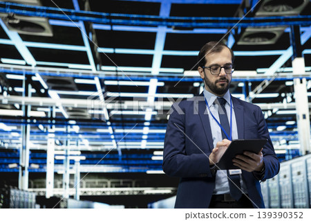 Data center technician using tablet to monitor system performance, identifying bottlenecks. Server farm IT expert using device to implement optimizations improving electronics efficiency Data center technician using tablet to monitor system performance, identifying bottlenecks. Server farm IT expert using device to implement optimizations improving electronics efficiency 139390352