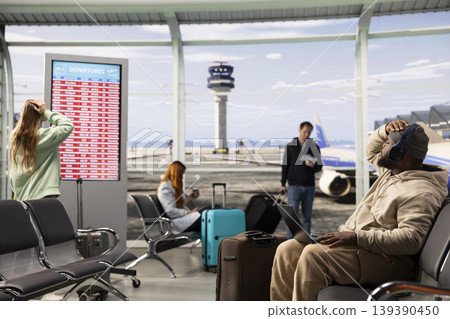 Unhappy black man worried about cancelled airplane departures, surrounded by other stranded upset passengers. Airport scene with red alert boards, bad news notifications and no boarding activity. Unhappy black man worried about cancelled airplane departures, surrounded by other stranded upset passengers. Airport scene with red alert boards, bad news notifications and no boarding activity. 139390450