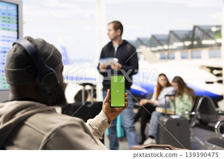 Vertical chroma key on phone with digital nomad beside carry-on luggage in the airport terminal, waiting for boarding and departure. Holiday travel for location independence and mobile culture. Vertical chroma key on phone with digital nomad beside carry-on luggage in the airport terminal, waiting for boarding and departure. Holiday travel for location independence and mobile culture. 139390475