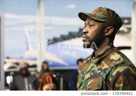 Close up of military man waiting in busy airport lounge for plane arrival. African american army soldier enduring long flight layover before next airplane departure in transit hub Close up of military man waiting in busy airport lounge for plane arrival. African american army soldier enduring long flight layover before next airplane departure in transit hub 139390481