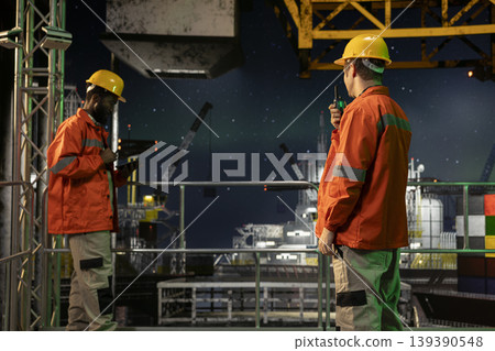 Offshore drilling rig engineer speaking through walkie talkie with colleagues, monitoring oil extraction systems for efficiency. Trying to minimize carbon footprint levels on platform. Offshore drilling rig engineer speaking through walkie talkie with colleagues, monitoring oil extraction systems for efficiency. Trying to minimize carbon footprint levels on platform. 139390548