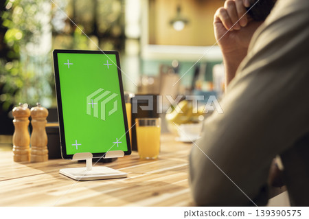 Vertical green screen on tablet with adult working remotely in the kitchen, focused on data analytics and information research on gadget. Teleworking lifestyle highlights productivity during daytime. 139390575