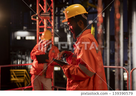 African american engineer exchanges insights on walkie talkie from drilling platform, coordinating fuel and natural petroleum extraction on offshore oil rig. Efficient fossil fuels production. African american engineer exchanges insights on walkie talkie from drilling platform, coordinating fuel and natural petroleum extraction on offshore oil rig. Efficient fossil fuels production. 139390579