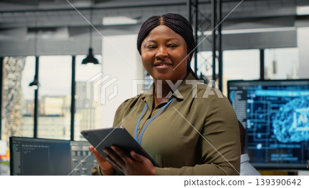 Portrait of smiling engineer working in office, using specialized hardware to accelerate complex AI calculations. Happy woman managing systems for machine learning training datasets, camera B 139390642