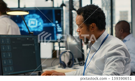 Technician in office solving tasks with artificial intelligence LLM chatbot answering prompts. African american man at work using PC to interact with large language model program, camera B Technician in office solving tasks with artificial intelligence LLM chatbot answering prompts. African american man at work using PC to interact with large language model program, camera B 139390651
