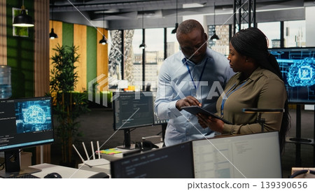 Engineers in startup office work with artificial intelligence driving market innovation. African american tech agency coworkers apply machine learning to optimize operations and efficiency, camera A 139390656