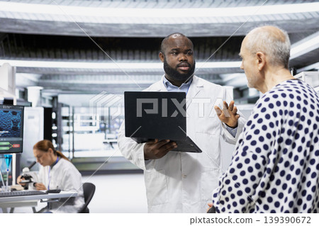 Black male doctor monitoring vitals and side effects on older man for new treatment testing to combat illness, examining possible chemical reaction or other symptoms. Medical progress. Black male doctor monitoring vitals and side effects on older man for new treatment testing to combat illness, examining possible chemical reaction or other symptoms. Medical progress. 139390672