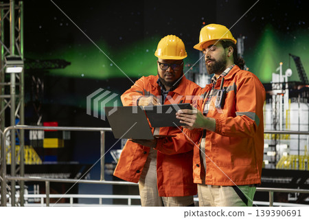 Drilling rig professionals managing operational workflows using laptop under green arctic lights. Offshore fossil fuel extraction platform workers document hazard reports after safety inspection Drilling rig professionals managing operational workflows using laptop under green arctic lights. Offshore fossil fuel extraction platform workers document hazard reports after safety inspection 139390691