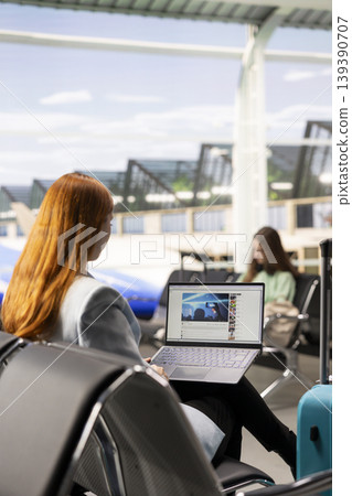 Woman watching streaming video content in airport departure lounge, enjoying online media and entertainment while waiting for her flight. Highlights the use of streaming vlogs as a pastime. Woman watching streaming video content in airport departure lounge, enjoying online media and entertainment while waiting for her flight. Highlights the use of streaming vlogs as a pastime. 139390707