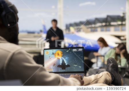 Excited gamer playing online competition game in airport terminal, strategy and interactive action while waiting plane. Modern travel moment with gaming as relaxation and entertainment. Excited gamer playing online competition game in airport terminal, strategy and interactive action while waiting plane. Modern travel moment with gaming as relaxation and entertainment. 139390724