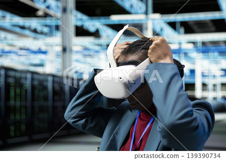 Putting VR headset on, industry standards compliance and programmer in data center overseeing equipment. Monitoring rigs efficiency, virtual reality tech and worker in server hub Putting VR headset on, industry standards compliance and programmer in data center overseeing equipment. Monitoring rigs efficiency, virtual reality tech and worker in server hub 139390734