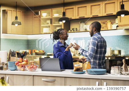 Smiling black man and woman sharing a romantic dance in the kitchen, waltzing together on a passionate love song and flirting with each other. Holding hands and slow dancing, swaying. 139390757