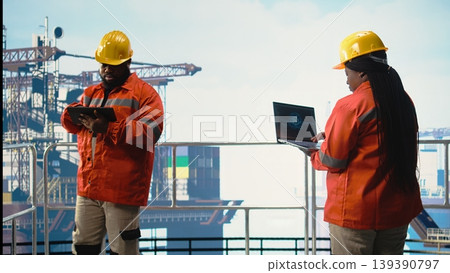 Engineer on offshore platform deck using artificial intelligence software on laptop to optimize drilling operations. Teamworking colleagues monitoring barge activity using AI technology, 139390797