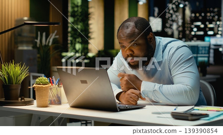 Male business manager leaning on desk showing symptoms of burnout and weariness. Sleep deprivation and work tension pushing limits with career difficulty and constant pressure. Male business manager leaning on desk showing symptoms of burnout and weariness. Sleep deprivation and work tension pushing limits with career difficulty and constant pressure. 139390854