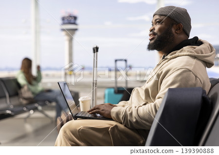 Black man digital nomad working on laptop in busy airport terminal lounge, modern remote professional illustrates location independent work and global mobility. Ability to work anywhere. Black man digital nomad working on laptop in busy airport terminal lounge, modern remote professional illustrates location independent work and global mobility. Ability to work anywhere. 139390888