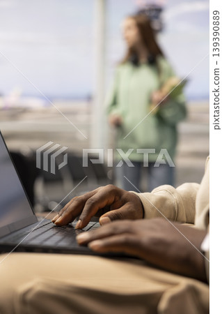 African american connected traveler in busy airport terminal lounge, typing on laptop and waiting for boarding flight. Modern digital nomad job and flexible career with travel lifestyle. African american connected traveler in busy airport terminal lounge, typing on laptop and waiting for boarding flight. Modern digital nomad job and flexible career with travel lifestyle. 139390889