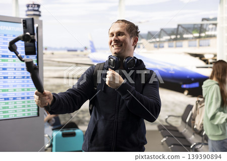 Solo male traveler, recording video blog, in airport terminal lounge, sharing travel tips and holiday experiences with online audience. Influencer culture, and the freedom of content creation. 139390894