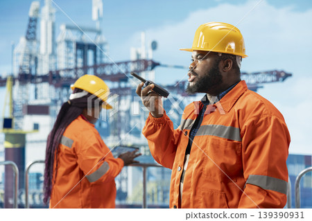 Drilling rig specialist uses two way radio to establish communication with logistics crew. Offshore installation manager speaks in walkie talkie providing audio clarity in noisy environment 139390931