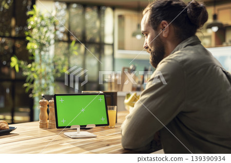 Mockup green screen on tablet in the kitchen with natural light, wooden table at home. Adult male looking at chroma key display and working remotely. Multitasking and telecommuting. Mockup green screen on tablet in the kitchen with natural light, wooden table at home. Adult male looking at chroma key display and working remotely. Multitasking and telecommuting. 139390934