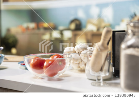 Comfortable kitchen setup with pizza ingredients on a modern countertop. Bowls of tomatoes and mushrooms beside spices and kitchenware, ready for a fun weekend activity of cooking. Comfortable kitchen setup with pizza ingredients on a modern countertop. Bowls of tomatoes and mushrooms beside spices and kitchenware, ready for a fun weekend activity of cooking. 139390943
