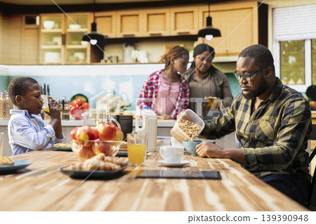 Parents and children starting the day with a healthy breakfast of pastry and eggs, cozy morning light in the kitchen. Family bonding, warmth and the joy of sharing delicious food together. 139390948