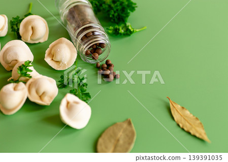 Raw tortellini pasta with spices and herbs on green background Raw tortellini pasta with spices and herbs on green background 139391035