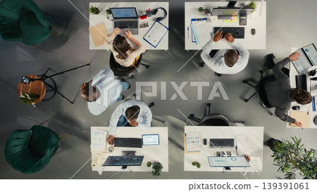 Top down view of diverse staff recording marketing ad for web advertisement in office, broadcasting live while coworkers solve their business tasks for productivity. 139391061