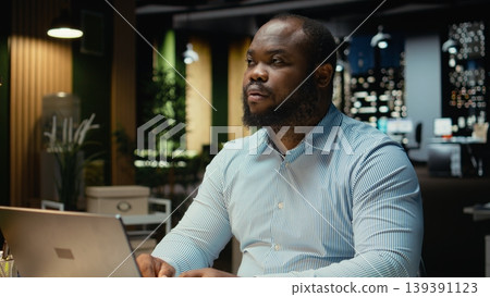 Black employee engages in methodical planning at night in corporate workspace, projecting new ideas and reflecting on business outlooks to find solutions for a challenging problem. Black employee engages in methodical planning at night in corporate workspace, projecting new ideas and reflecting on business outlooks to find solutions for a challenging problem. 139391123