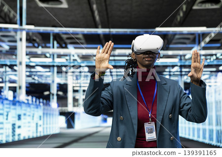 Data center female programmer using VR headset gear to configure server settings. IT specialist in modern high tech server hub uses virtual reality technology to do maintenance tasks on infrastructure Data center female programmer using VR headset gear to configure server settings. IT specialist in modern high tech server hub uses virtual reality technology to do maintenance tasks on infrastructure 139391165
