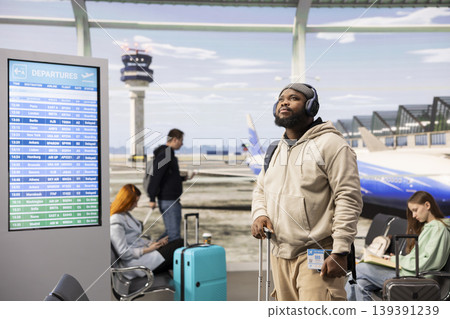 African american traveler checking flights information in busy airport terminal, wearing backpack and waiting near the gate. Passengers waiting in the lounge area, checking flight details. African american traveler checking flights information in busy airport terminal, wearing backpack and waiting near the gate. Passengers waiting in the lounge area, checking flight details. 139391239